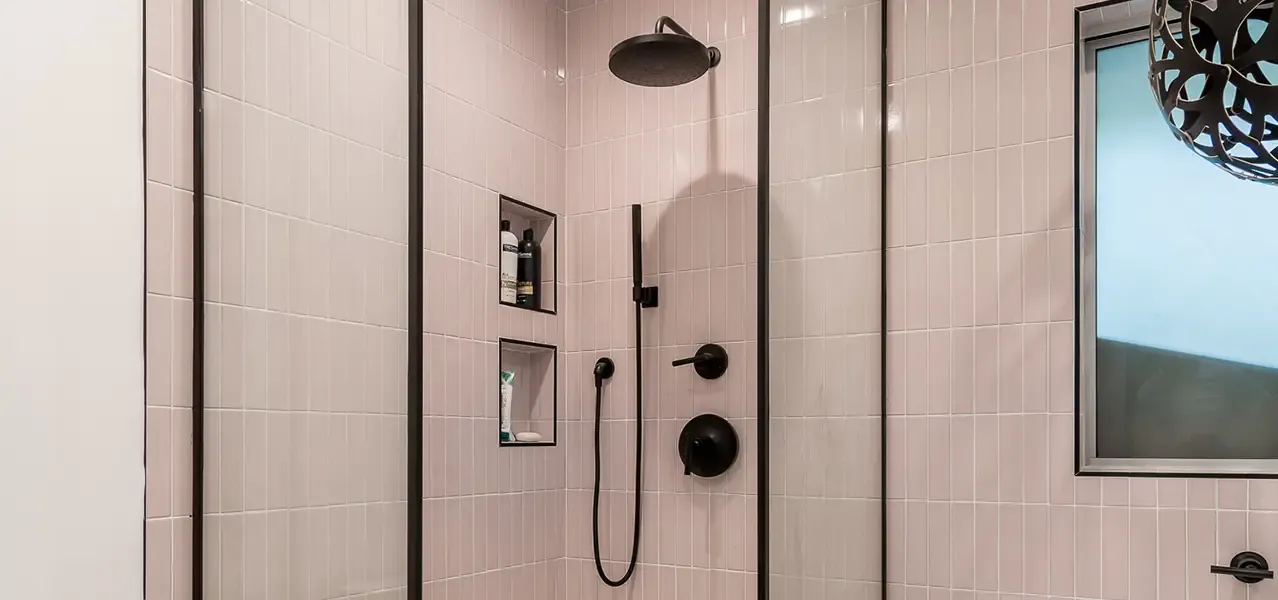 Modern bathroom shower with soft pink tiles, black fixtures, and a large window.