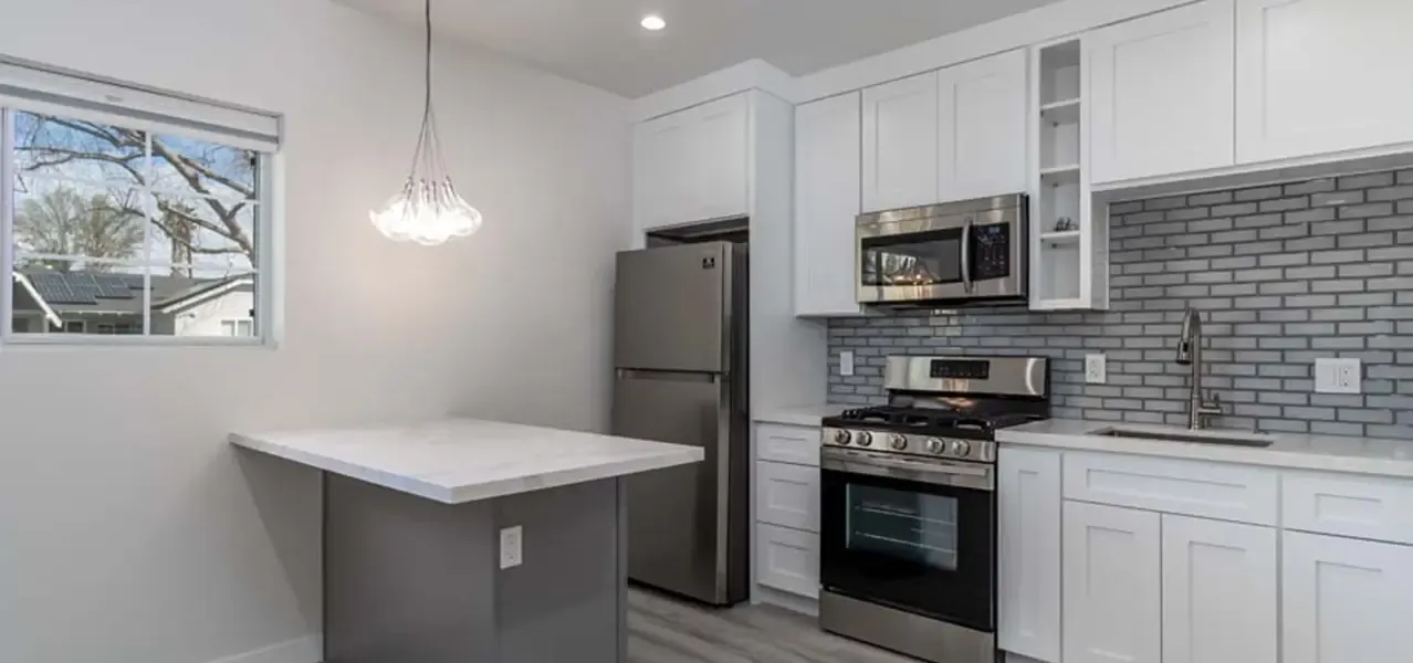 A modern kitchen with white cabinetry, stainless steel appliances, grey subway tile backsplash, and a kitchen island with pendant lighting