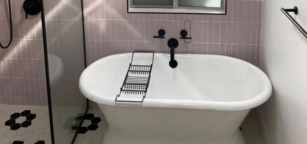 Modern bathroom with white freestanding tub, pink tiles, and black fixtures.
