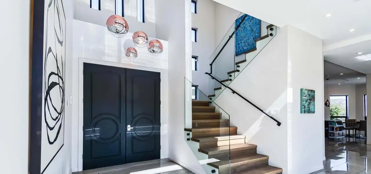 A modern entryway with dark blue double doors, glass staircase, wooden steps, and abstract wall art