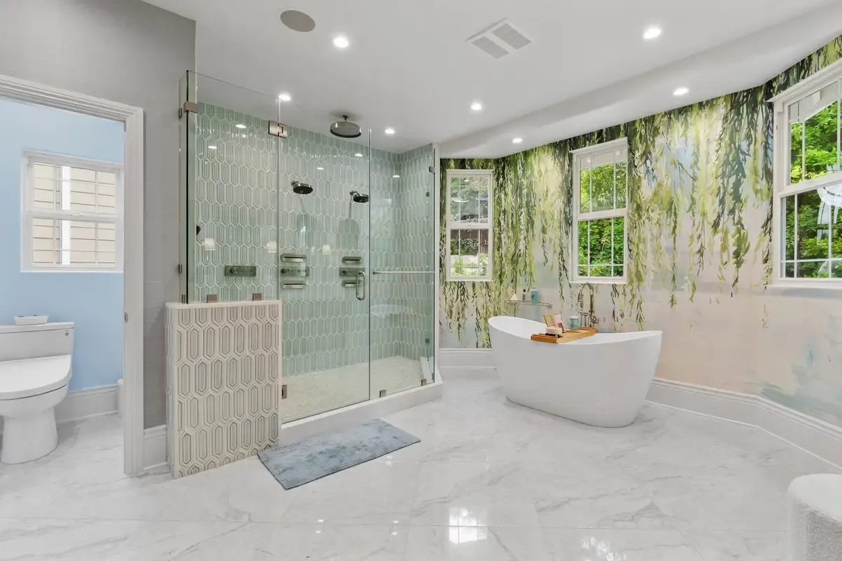 A spacious, modern bathroom with a luxurious design featuring a glass-enclosed shower with hexagonal tile, a freestanding white bathtub, and nature-inspired wallpaper.